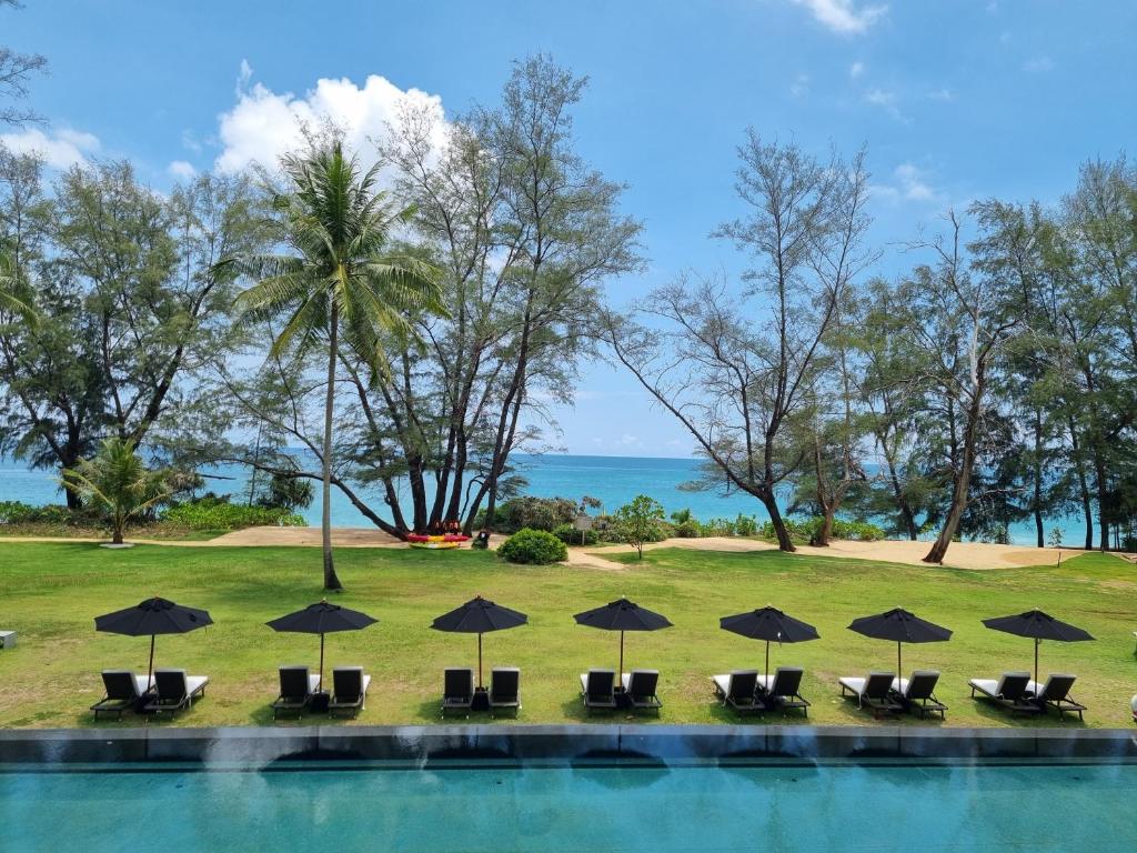 a pool with chairs and umbrellas and the ocean at SALA Phuket Mai Khao Beach Resort - SHA Plus in Mai Khao Beach
