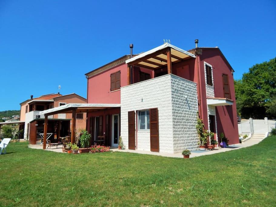 uma grande casa vermelha com um relvado verde em frente em Appartamento Valentina: relax e natura em Sirolo
