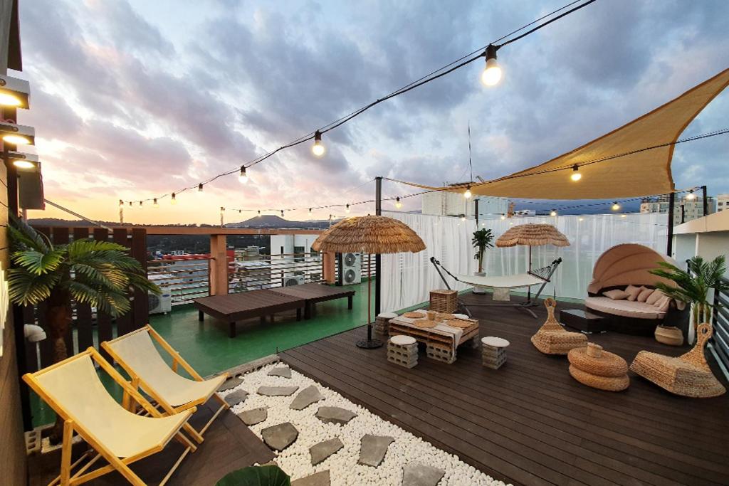 d'une terrasse avec des chaises, des tables et des parasols sur le balcon. dans l'établissement HY Choi Hostel, à Seogwipo