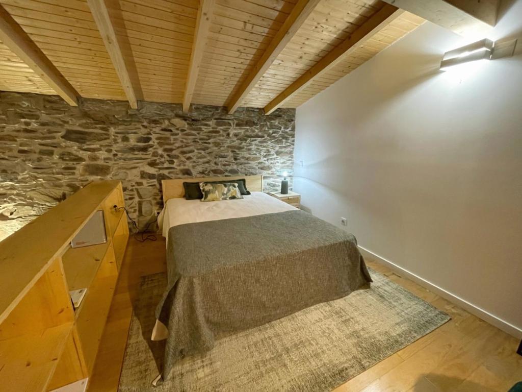 1 dormitorio con cama y pared de piedra en acalma - sesmo, en Sarzedas