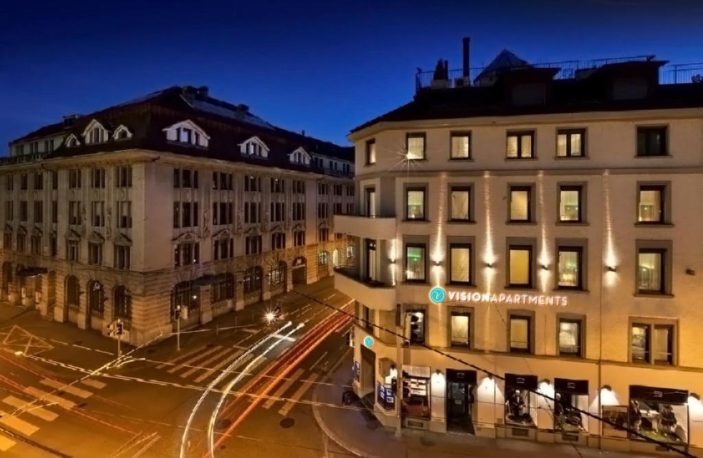 una calle de la ciudad por la noche con edificios y luces en Stay2Night BS, en Zúrich