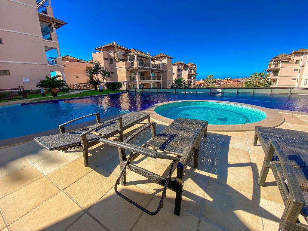 a pool with two benches in front of some buildings at Beverly Hills por Be My Guest in Aquiraz