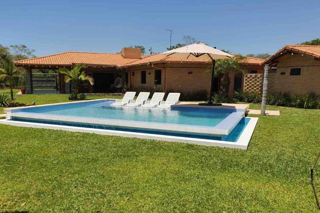 a swimming pool with white chairs and a house at Casa con Piscina, Quincho, Cancha de Futbol/Volley in San Bernardino