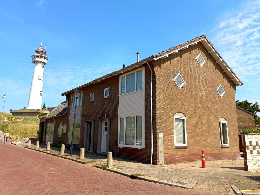 a brick building with a lighthouse in the background at 't Zwanennest Egmond aan Zee in Egmond aan Zee