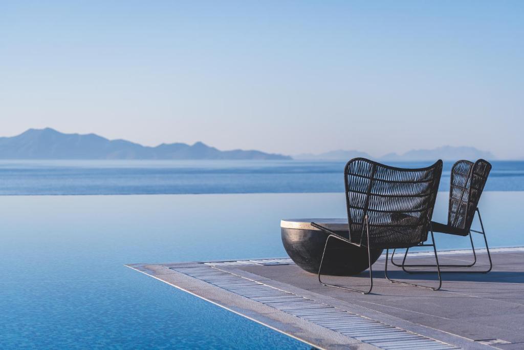 due sedie sedute accanto a un corpo d'acqua di Michelangelo Resort & Spa ad Ágios Fokás