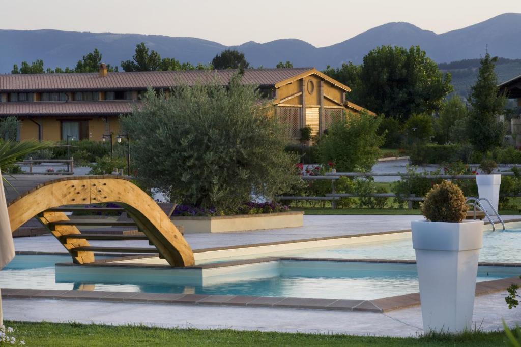 un puente de madera sobre una piscina con montañas al fondo en Il Baio Relais & Natural Spa, en Camporoppolo