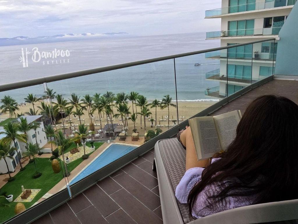 a woman sitting on a balcony reading a book at Icon Vallarta Beach front By Bamboo Skylife in Puerto Vallarta