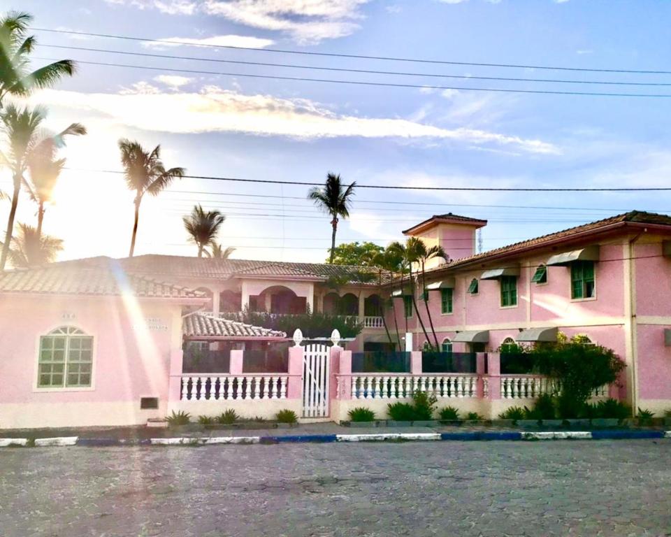 a pink house with a white fence and palm trees at Pousada Villa Rosada in Santa Cruz Cabrália