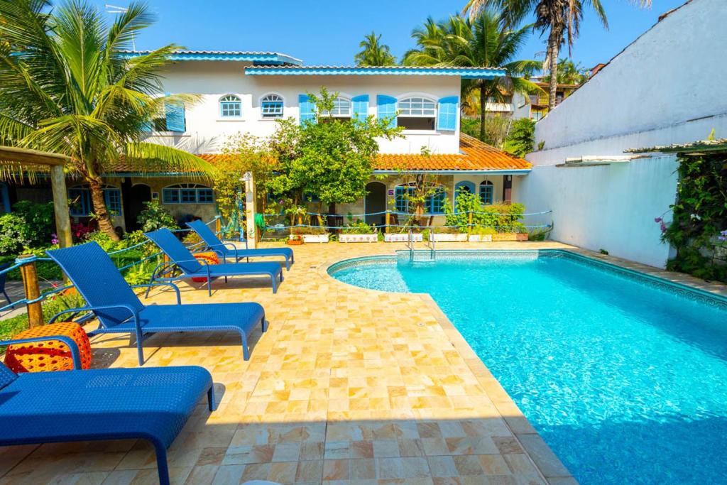 uma piscina com cadeiras azuis e uma casa em Barlavento Villas em Ilhabela