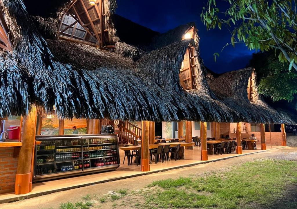 un restaurante con techo de paja, mesas y sillas en Arca Tayrona Restaurant & Hostal en Santa Marta
