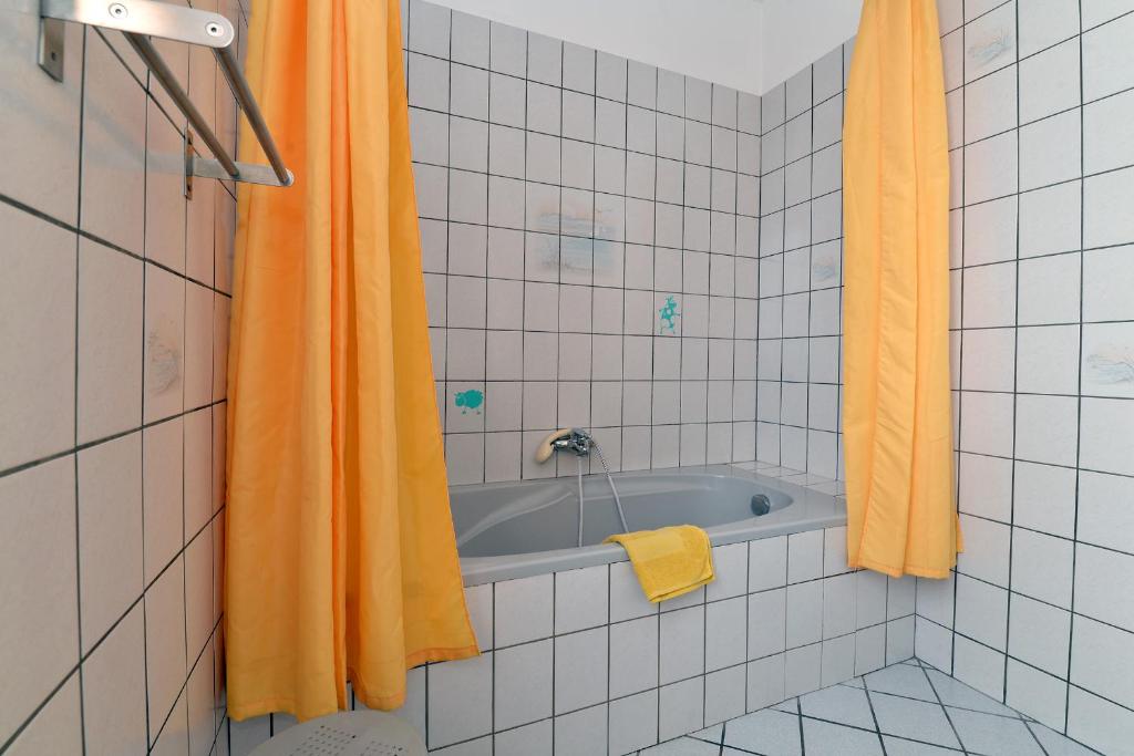 a bathroom with a tub with an orange shower curtain at S&#39;Harzala Jaune in Bergheim