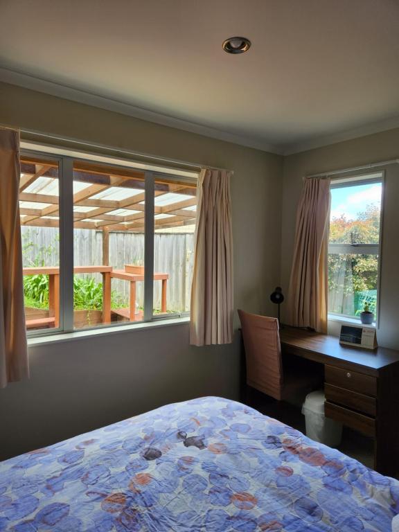 a bedroom with a bed and a desk and windows at Sweet home in Albany in Auckland