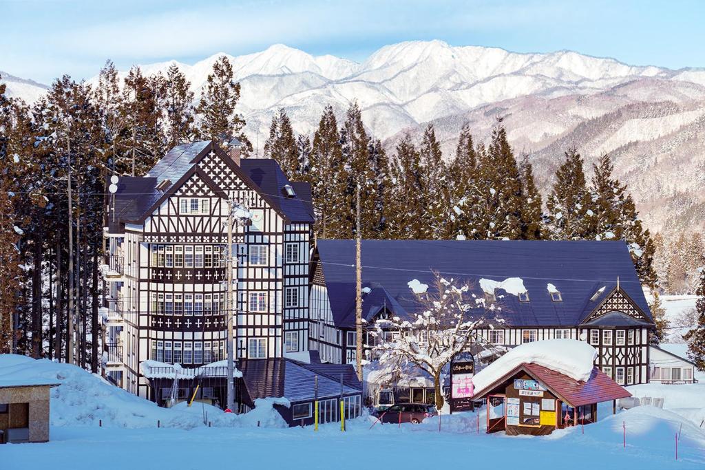 a building in the snow with mountains in the background at Hakuba Sun Valley Hotel Annex in Hakuba