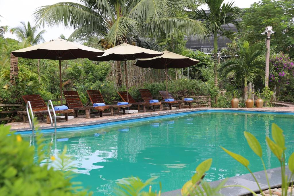 a swimming pool with chairs and umbrellas next to it at Vamxang Rustic Home in Can Tho