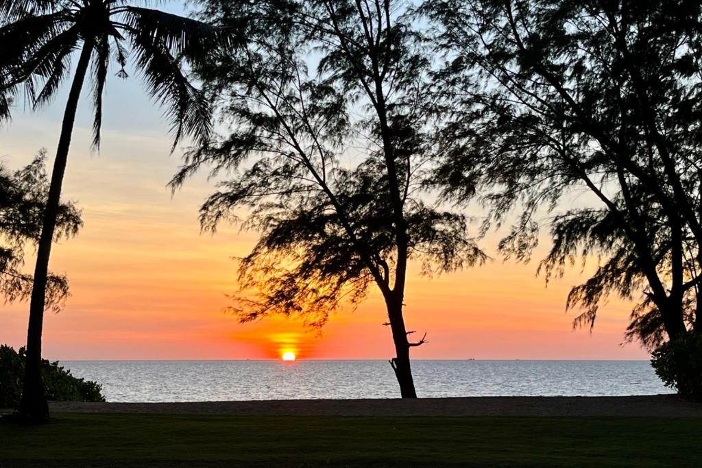 um pôr-do-sol sobre o oceano com palmeiras em Baan Mai Khao - 2 Bedroom Luxury Condo- Direct Pool & Beach Access em Mai Khao Beach