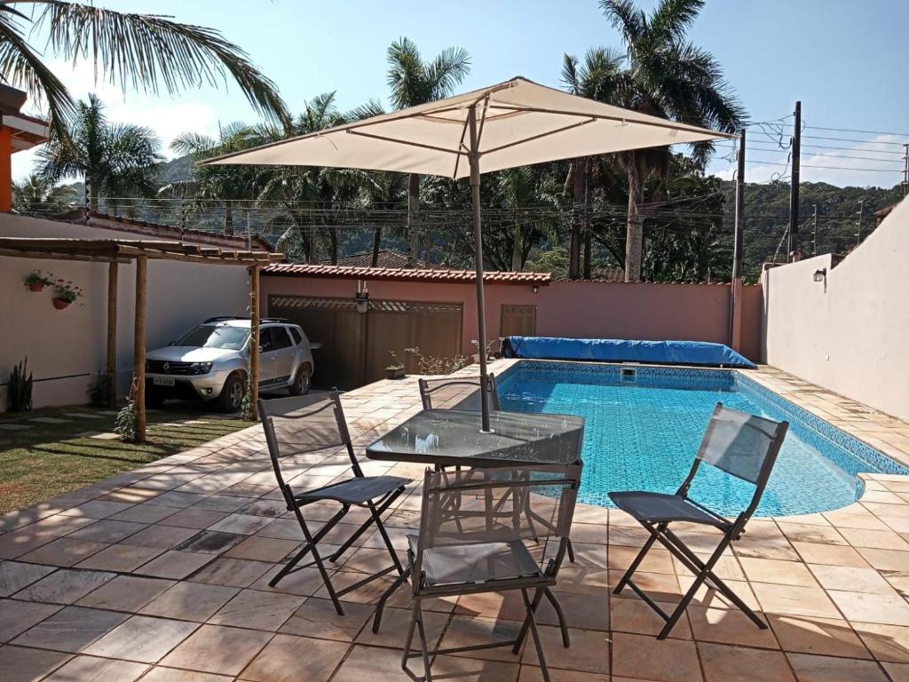 uma mesa e cadeiras com um guarda-sol ao lado de uma piscina em Refúgio BEM-TE-VI no Guarujá