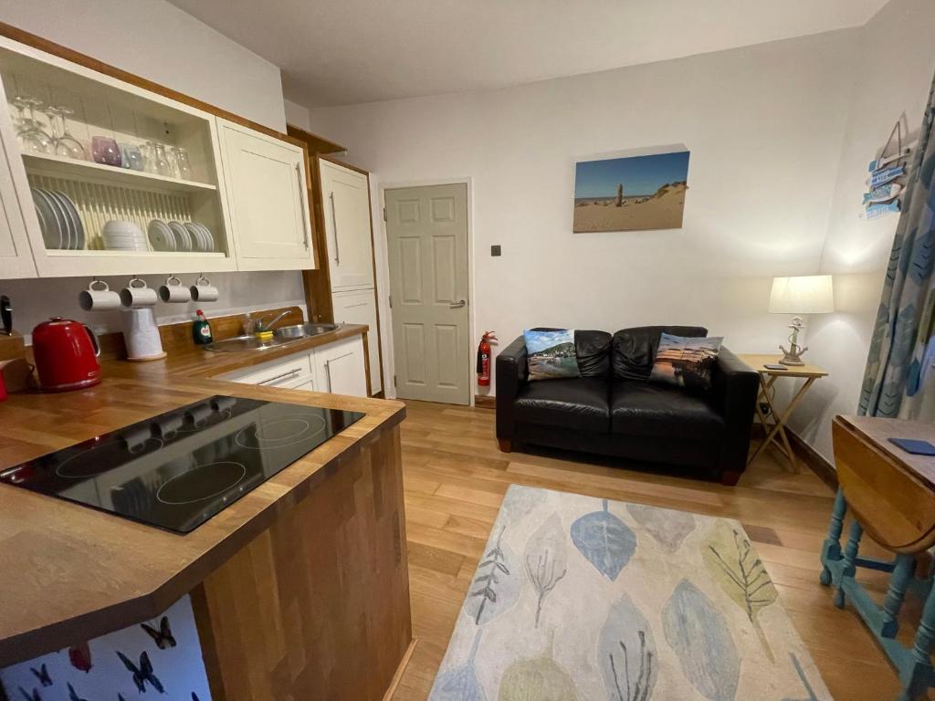 a kitchen and living room with a black leather couch at Flat 2, Ty Newydd in Barmouth