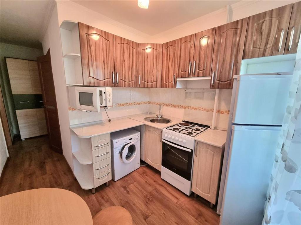 eine kleine Küche mit Holzschränken und einem weißen Kühlschrank in der Unterkunft 1-комн центр, 45 квартал, Вокзал, Бухар-Жырау 69 in Qaraghandy