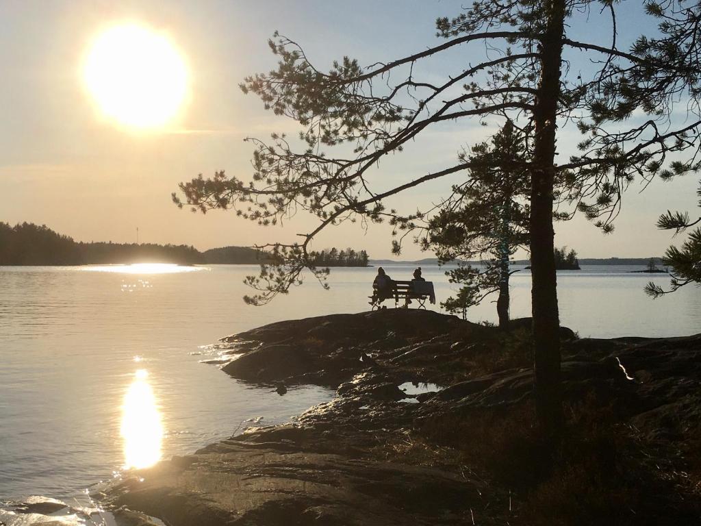 dos personas sentadas en un banco frente a un lago en Casino Islands Retreat, en Savonlinna