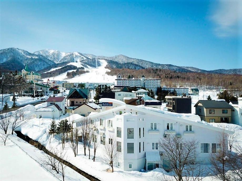 un edificio blanco en la nieve con una ciudad en FURANO B&B en Furano