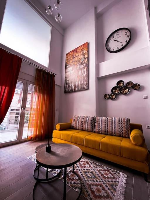 a living room with a yellow couch and a clock at Escala Luxury Loft 2 in the center &Free Parking in Volos