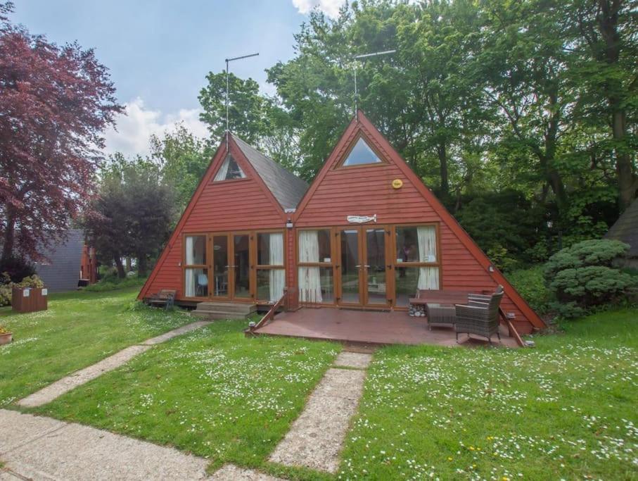 een rood huis met een bank in een tuin bij Pebbles Seaside Lodge in Kent