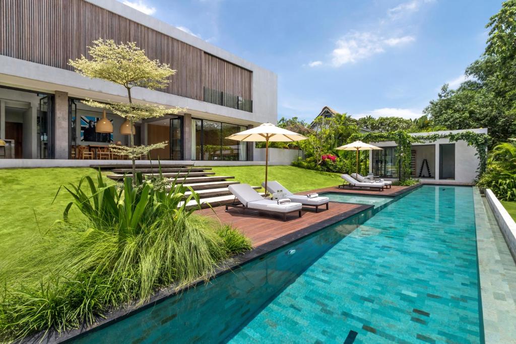 a pool with chairs and umbrellas next to a building at Villa Oasis Bali in Dalung