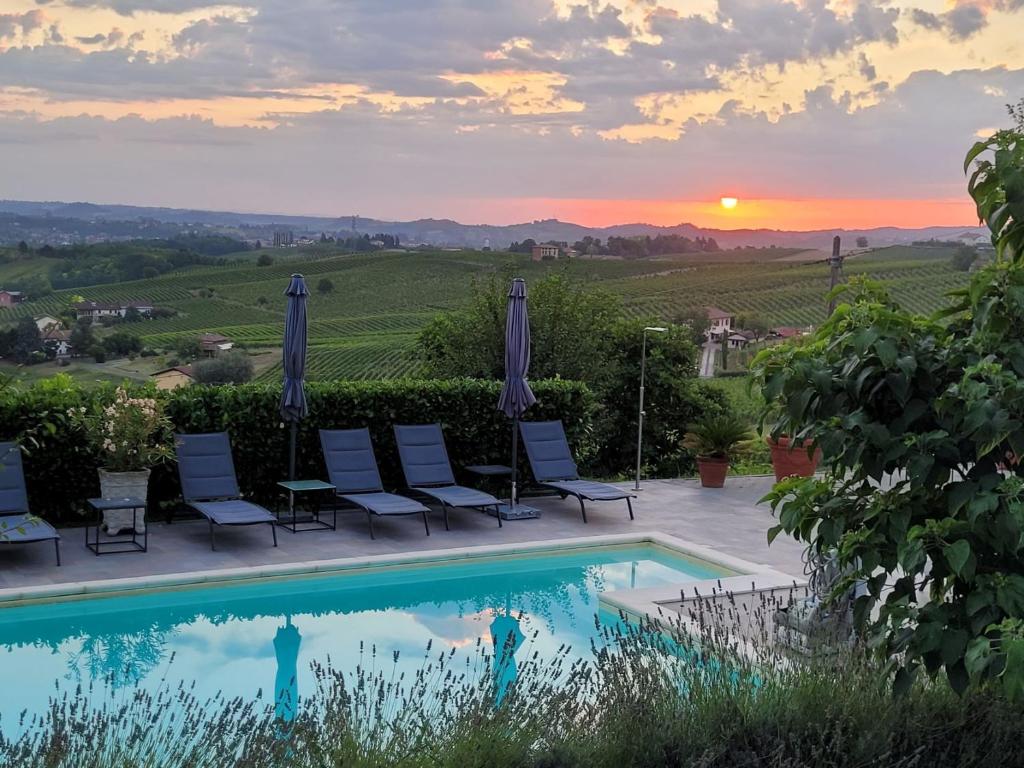 a pool with chairs and the sunset in the background at Villa Bella Piemonte in Nizza Monferrato