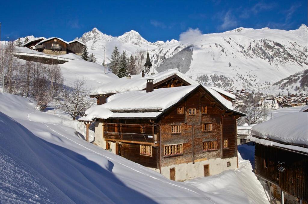 a wooden building covered in snow with mountains in the background at Alpenlodge Tgèsa Surrein Giassa10 in Sedrun