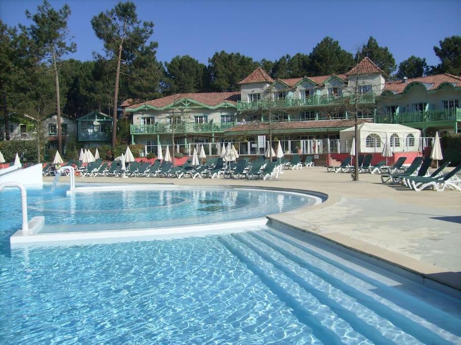 une piscine dans un complexe hôtelier avec chaises et parasols dans l'établissement La Pinède Golf, Surf, Vélo, Piscine, à Lacanau