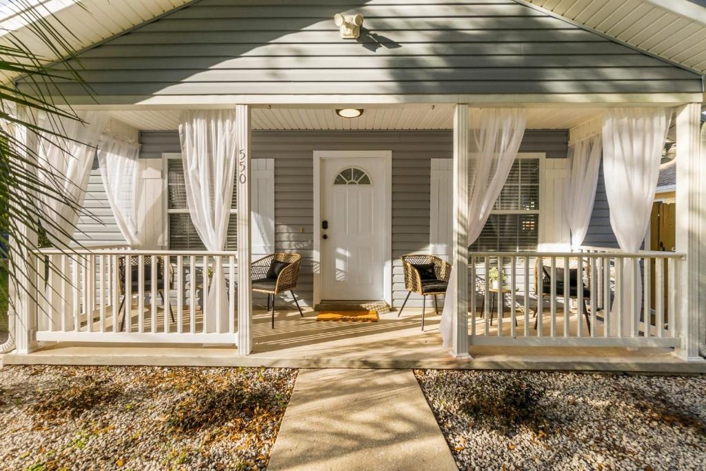 ein Haus mit einer Veranda mit Stühlen und Vorhängen in der Unterkunft Boho Bungalow - Chic Pet Friendly Mins to Town in St. Augustine