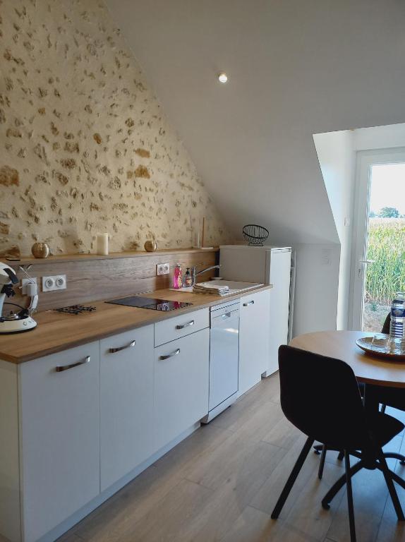 une cuisine avec des armoires blanches, une table et une fenêtre dans l'établissement Gîtes & SPA du bien-être - Logement cosy à la campagne - ACCES SPA EN SUPPLEMENT, à Courgains