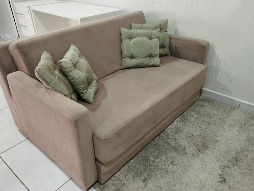 Un sofá marrón con tres almohadas encima. en Ap flat central- ar, garagem e ótima localização, en Foz do Iguaçu