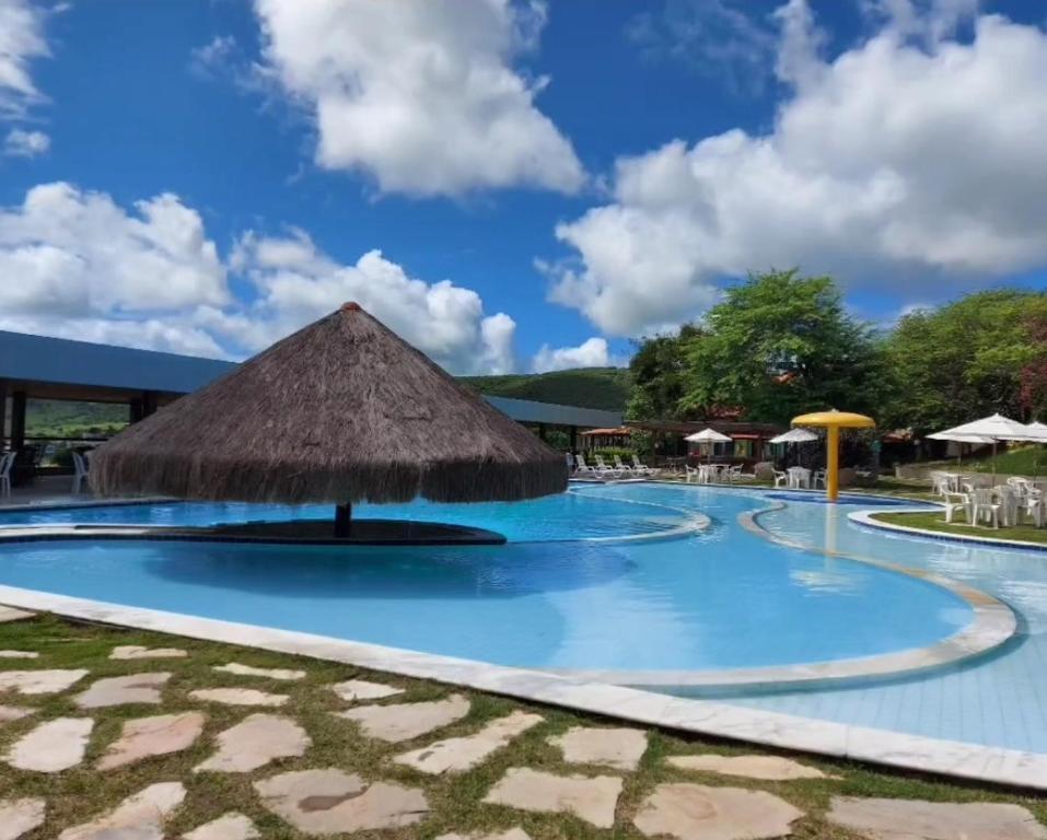a resort swimming pool with a thatch roof at Flat aconchegante em Hotel Fazenda Monte Castelo in Gravatá