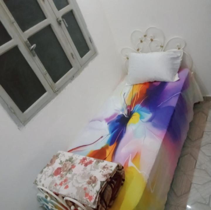 a multicolored bed with a pillow and a chair at غرفة فردية خاصة للاناث in Bel Aroussi