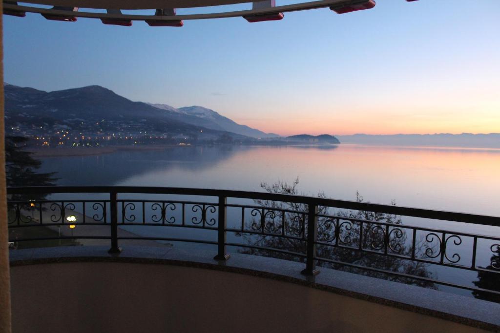 Balcony with wrought-iron railing overlooking calm lake at dusk, distant town lights and a small island on the horizon at City Palace Hotel in Ohrid