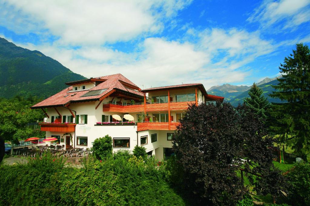 a building on a hill with mountains in the background at Hotel Haselried in Tirolo