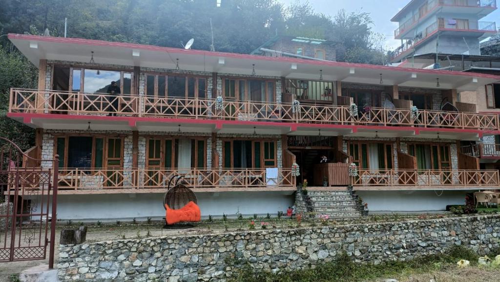 a house with a balcony and a stone wall at RRR RESORTS TIRTHAN Valley by RRR HOTELS & RESORTS in Banjār