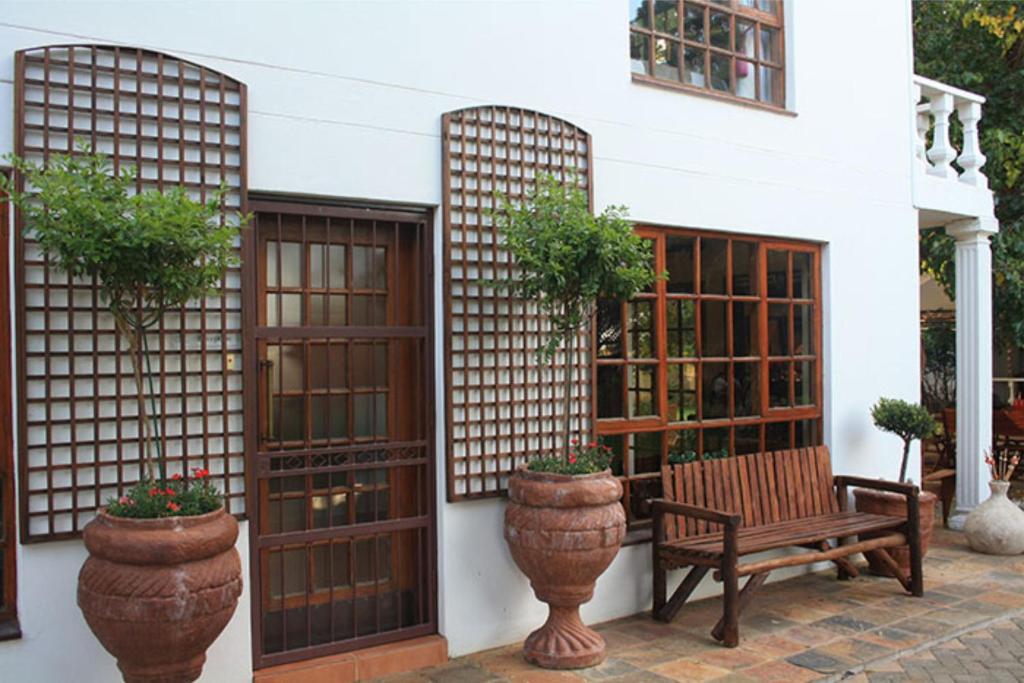 a bench sitting in front of a house with potted plants at De Stallen Guest Villas and Mashie Golf Course in Bloemfontein