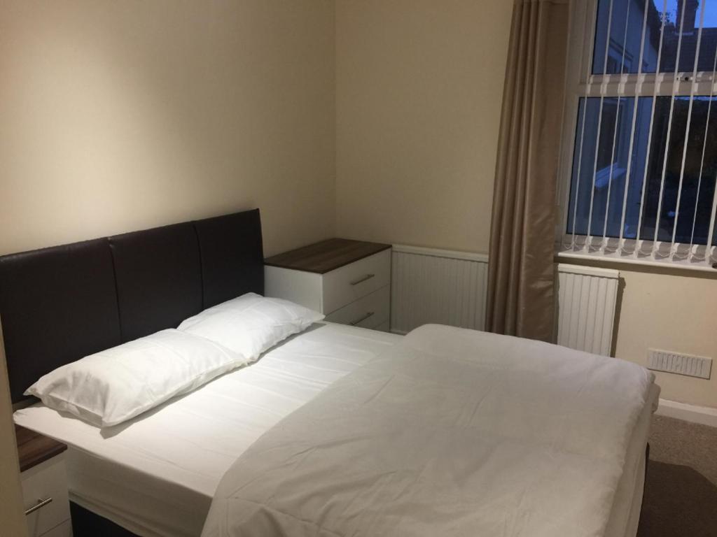 a bedroom with a bed with white sheets and a window at Duncan House in Leicester