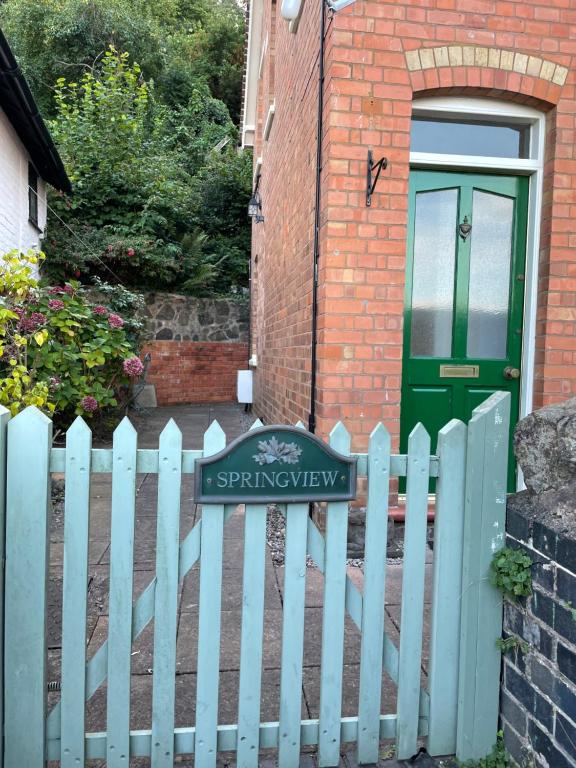 a white picket fence in front of a house with a green door at Spring View in Little Malvern