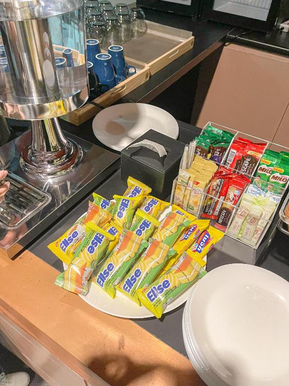 A self-service refreshment station with coffee, bottled drinks, packaged snacks and plates.