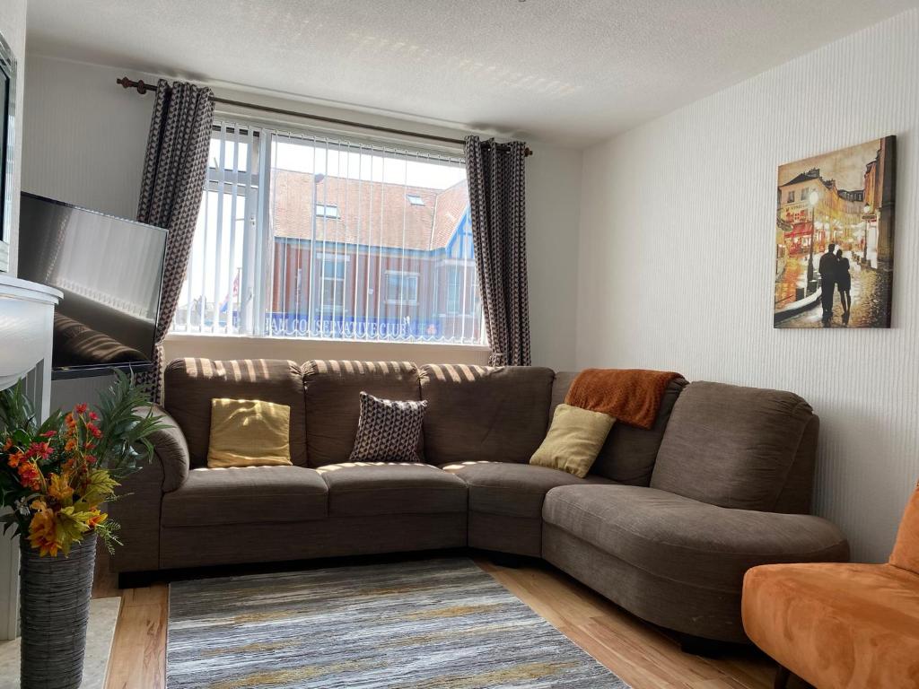 a living room with a brown couch in front of a window at M&J Apartment in Blackpool