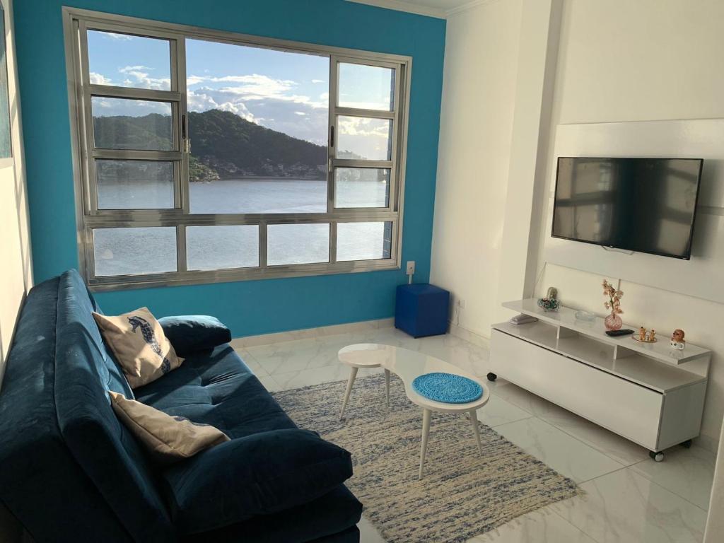 uma sala de estar com um sofá azul e uma grande janela em Cobertura Pé na Areia e Incrível Vista Para a Praia em São Vicente