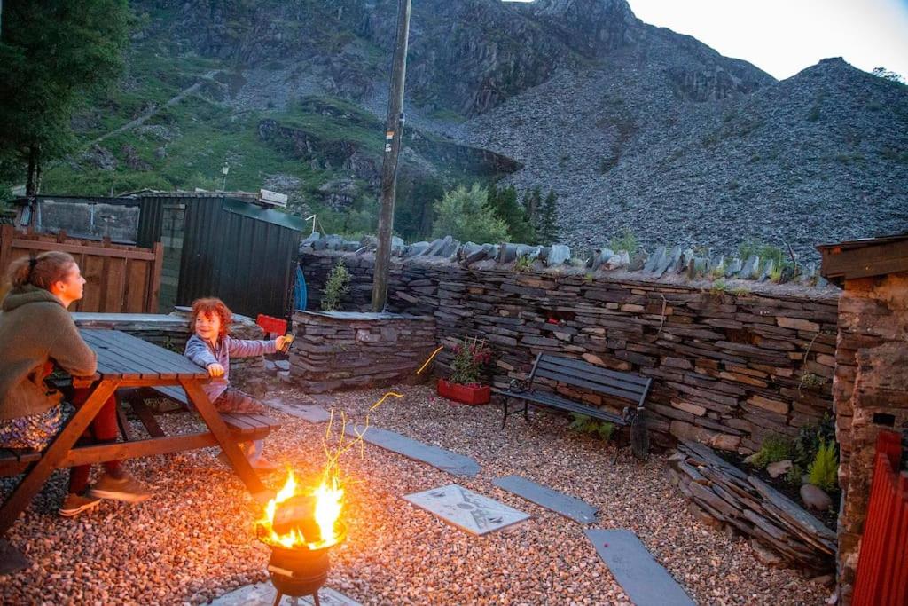 a man and a child sitting at a picnic table with a fire at Traditional 19th Century Slate Miners Cottage in Blaenau-Ffestiniog