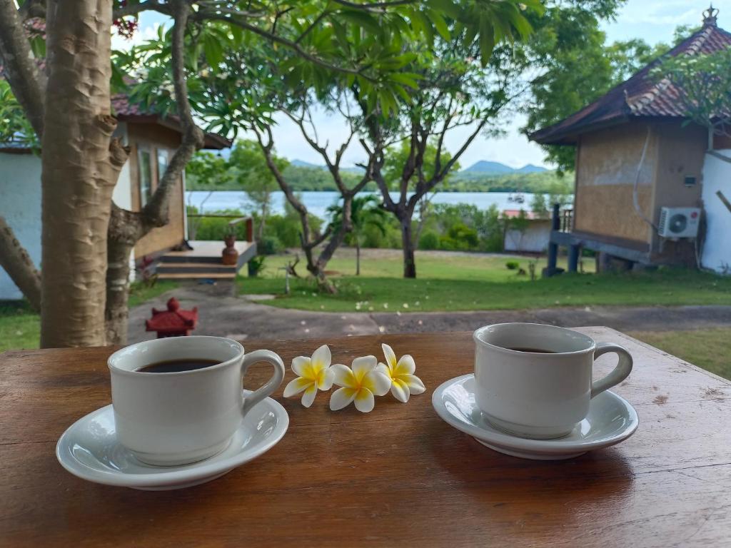 two cups of coffee on a wooden table with flowers at Pasir Putih Cottage - Menjangan in Banyuwedang