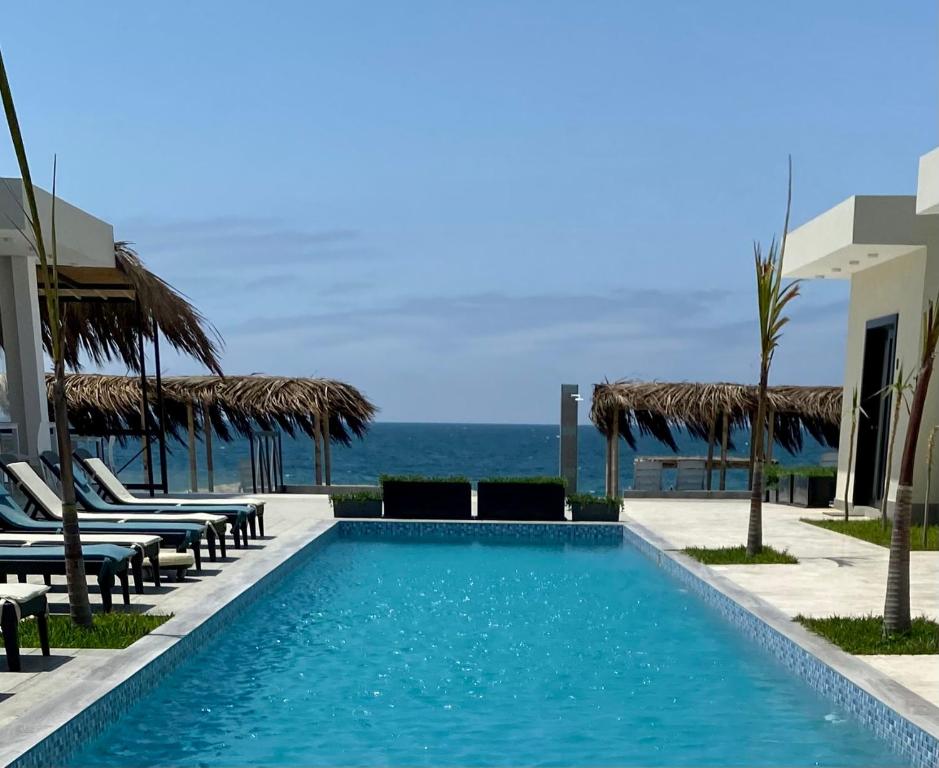 einen Pool mit Stühlen und das Meer im Hintergrund in der Unterkunft Riviera Vichayito in Vichayito
