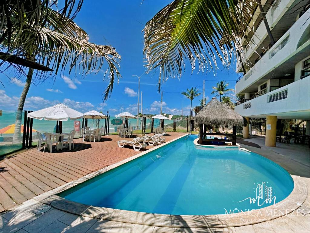 a swimming pool with chairs and umbrellas next to a building at DELUX BEIRA-MAR NATAL Flat in Natal