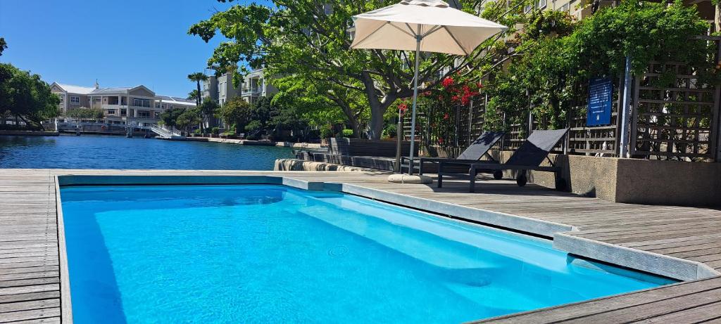 uma piscina com guarda-sol e cadeiras junto à água em V&A Waterfront Marina Family Apartment 101 Altmore em Cidade do Cabo