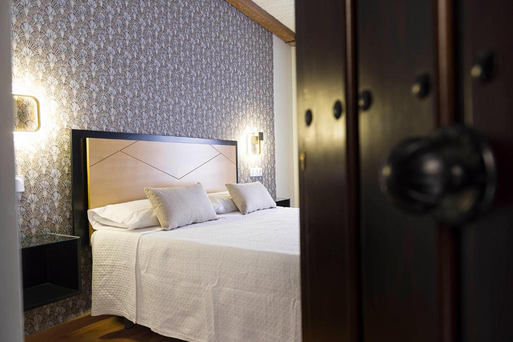 um quarto com uma cama com lençóis brancos e almofadas em Hotel Juancaballo em Úbeda